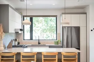 Kitchen view from the living area. Beautiful matte stone counters, custom handmade ceramic pendants, dimensional tile backsplash, pop up outlets. Baby seat that hooks to the counter available.