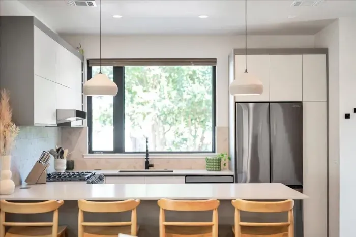 Kitchen view from the living area. Beautiful matte stone counters, custom handmade ceramic pendants, dimensional tile backsplash, pop up outlets. Baby seat that hooks to the counter available.