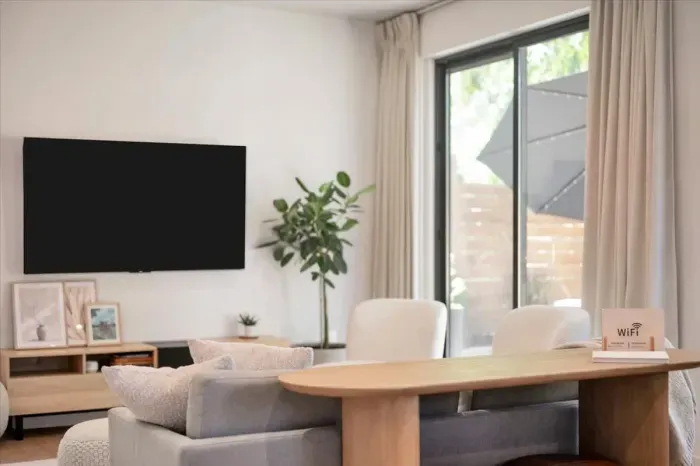 Living Room with TV and sound bar for pregame. Sliding door opens to outside patio. Oversized windows allow natural light and tall ceilings make the space feel expansive.