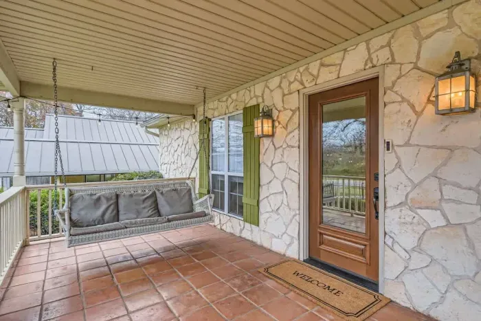 Welcome to your charming front porch retreat! This inviting space features a cozy swing perfect for morning coffee or relaxing evenings. With warm terracotta tile flooring, elegant stone accents, and glowing lantern-style sconces, swinging on the por