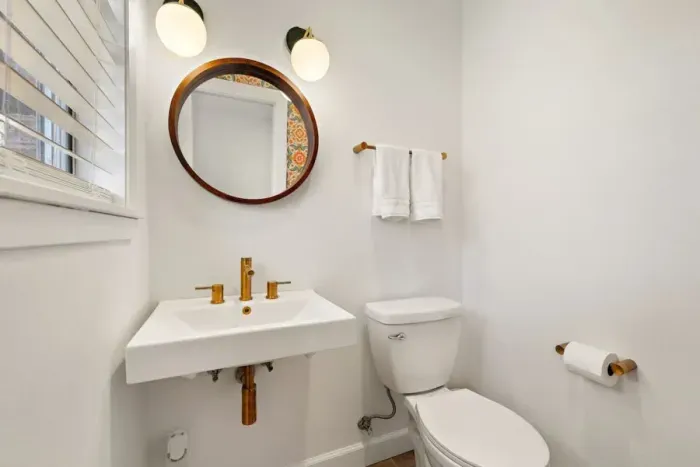 Trendy half bathroom featuring a sleek round mirror, adding a touch of elegance and style. The modern design creates a clean, functional space, perfect for guests. Simple yet sophisticated, this bathroom offers a welcoming atmosphere with a timeless