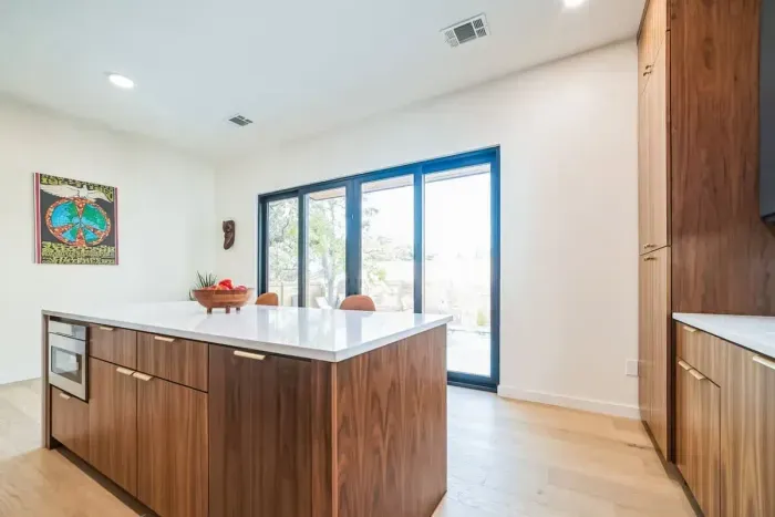This modern kitchen is a harmonious blend of style and functionality, featuring sleek countertops, state-of-the-art appliances, and minimalist cabinetry. A large window or sliding glass doors provide an uninterrupted view of the sparkling pool.