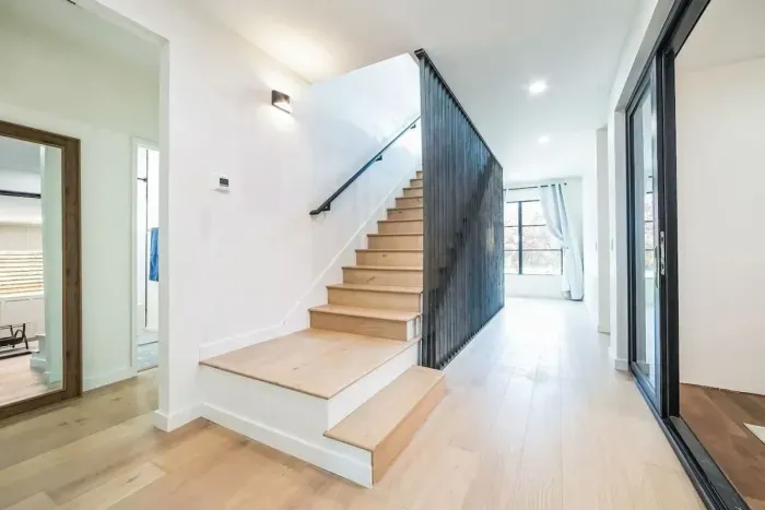 Step into this modern home with sleek wood flooring, a statement staircase, and large windows that fill the space with natural light. The clean design and warm accents create a welcoming ambiance, perfect for relaxing or entertaining.
