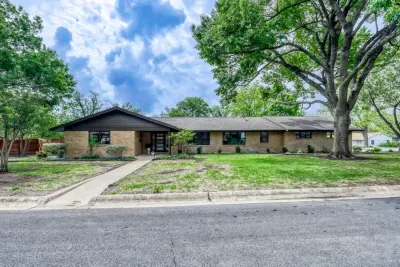 Spacious front yard and clean curb appeal, framed by towering shade trees in a quiet neighborhood