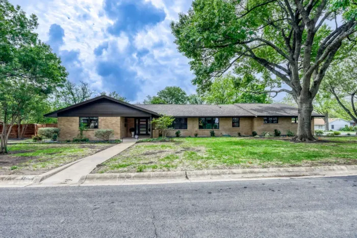 Spacious front yard and clean curb appeal, framed by towering shade trees in a quiet neighborhood