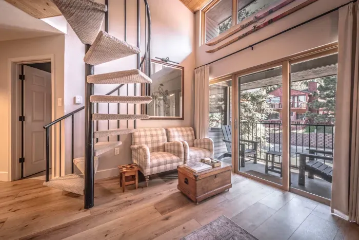 Bright living space with spiral staircase and forest-view windows.