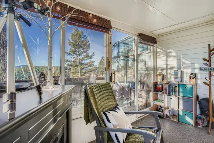 Bright sunroom with panoramic forest views and comfy seating.
