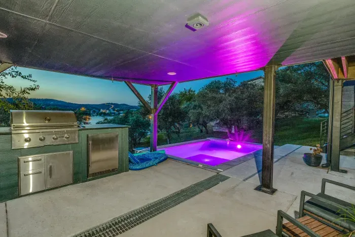 Covered outdoor kitchen and dining space with colorful evening lighting.