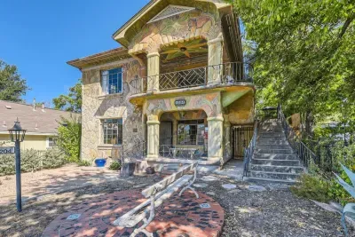 The house features a stunning exterior with a soft cream-colored facade, accented by rich brown wood trim and deep green shutters.Lush greenery and vibrant flowers surround the property, adding a pop of color against the neutral backdrop.