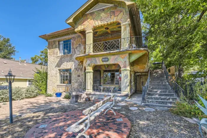 The house features a stunning exterior with a soft cream-colored facade, accented by rich brown wood trim and deep green shutters.Lush greenery and vibrant flowers surround the property, adding a pop of color against the neutral backdrop.