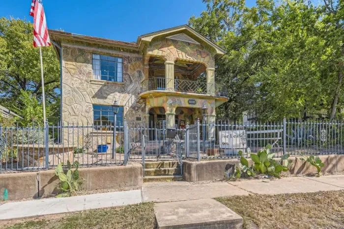 This beautiful home showcases a remarkable blend of artistic design and natural charm. The balcony, framed by sculpted stone pillars and intricate railings, provides an inviting space to relax while enjoying the vibrant scenery. The warm stone textur