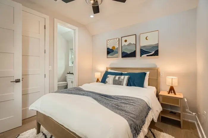 This minimalist room features a queen bed with crisp white linens, neutral decor, and a tranquil vibe for the perfect restful escape.