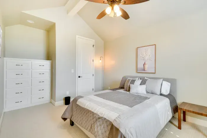 Bright guest bedroom with queen bed and ceiling fan.