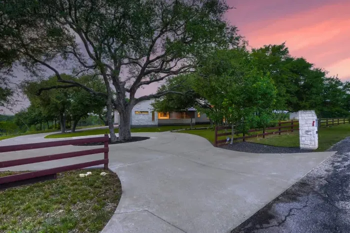 Grand driveway entrance shaded by mature trees.