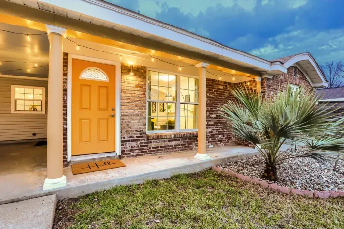 Bright and welcoming front entrance with landscaped palms and warm porch lighting