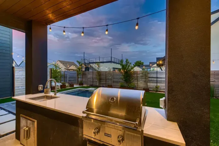 Backyard with outdoor sink & grill, artificial turf, pool, lights, and professional landscaping.