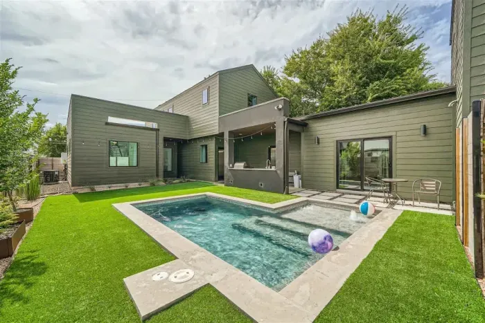 Backyard with artificial turf, pool, lights, and professional landscaping.