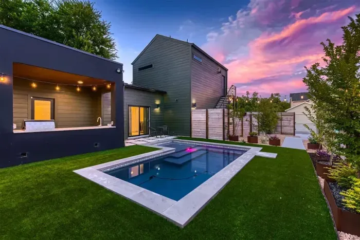 Backyard with artificial turf, pool, lights, and professional landscaping.