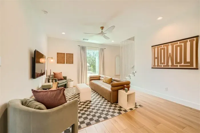 Relax in the bright and airy living room, featuring crisp white walls that create an open, welcoming space. The room is equipped with a flat-screen TV for entertainment, and the wooden-like tile flooring adds warmth and coziness.