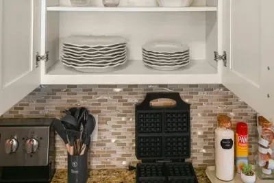 Well-appointed kitchen: Cabinets filled with plates and a waffle maker ready for breakfast on the counter.