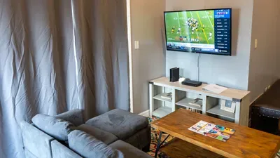 Game-Day Ready Living Area
Kick back in a cozy seating nook with plush gray loveseat, wood coffee table, and large smart TV perfect for sports, streaming, or movies, complete with media console and vibrant rug accents.