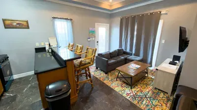 Spacious Living & Kitchen Combo
Gather in a welcoming open-plan space with comfy gray sofa, smart TV, granite breakfast bar with stools, and full kitchen, perfect for casual meals, family hangouts, or streaming beach evenings.