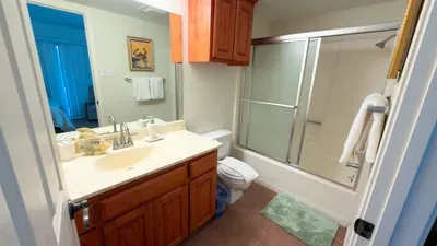 Bright, tidy bathroom featuring a clean vanity, organized storage, glass‑door tub, and fresh towels. Warm lighting and simple décor create a comfortable, well‑maintained space designed for convenience and a relaxing daily routine.