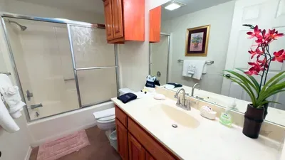 Clean, well‑kept bathroom featuring a bright vanity, organized storage, glass‑door tub, and fresh towels. Warm lighting and simple décor create a comfortable, functional space designed for easy routines and a relaxing stay.