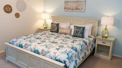 Unwind in this serene coastal-inspired bedroom featuring a comfy bed, plush pillows, and charming beachy décor. Soft blue hues and natural accents create a peaceful retreat—perfect for a restful night's sleep after a day in the sun.