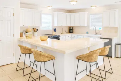 Bright, inviting kitchen featuring ample counter space, sleek white cabinetry, and modern appliances. Enjoy casual dining at the spacious breakfast bar with stylish wicker stools—perfect for morning coffee or entertaining guests in comfort.