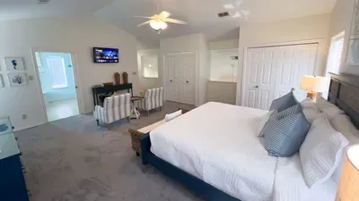 Spacious coastal master bedroom with plush serene bed, extra seating, and fresh blue-and-white décor. Enjoy relaxing with smart TV, ample closet space for the perfect blend of comfort and convenience.