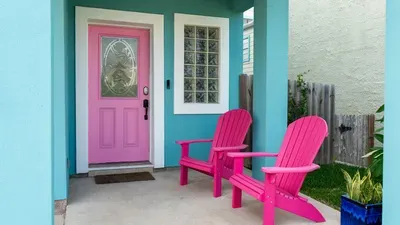 Welcome guests with vibrant coastal charm at this turquoise home entrance featuring a cheerful pink door and matching Adirondack chairs—perfect for relaxing outdoors and setting a warm, inviting mood right from the start.