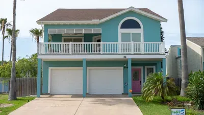 Welcome to this stunning turquoise beach house, perfectly lit for evening relaxation. Enjoy spacious balconies, double garage, lush palm landscaping, and a stylish pink front door—ideal for coastal living just steps from the shore!