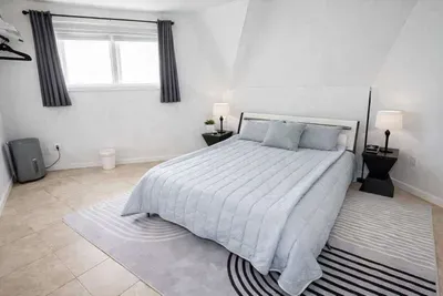 Modern minimalist bedroom retreat featuring a comfy bed with soft gray tones, geometric rug, and natural light. Thoughtfully styled for comfort and simplicity, ideal for guests seeking a clean, serene stay with contemporary design and cozy ambiance.