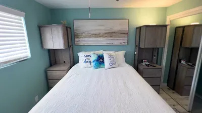 Wake up refreshed in a tranquil bedroom featuring a plush bed, soothing coastal hues, custom cabinetry, and nautical-inspired decor. Enjoy restful nights and the perfect ambiance for relaxation in your serene beach retreat.
