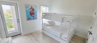 Sunlit bunkroom with plush white bedding and seamless access to a private balcony framed by palms. A bright, open space designed for effortless relaxation.