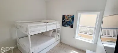 Bright bunk room with clean white bedding, playful astronaut art, and natural light flowing in from the balcony. A cozy, modern space perfect for kids or extra guests, designed for comfort and convenience.
