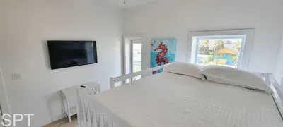 Coastal‑chic bedroom featuring white furnishings, warm wood tones, and floor‑to‑ceiling balcony doors. A serene, comfortable space for restful nights.