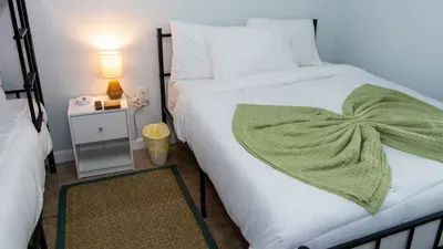 Nautical Bunk Room with Paddle Accents
Cool black bunk bed draped in green throw, nautical oars & paddle decor on walls. Gold sheer curtains, dresser, lamp, plant—fun, beachy vibe for kids. Perfect lower level sleep spot at Royale Beach & Tennis.