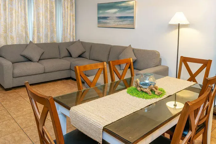 Cozy Living & Dining Retreat
Plush gray L-shaped sectional anchors airy living space with sea art, lamp glow, sheer drapes. Rustic wood table seats 6, adorned with coral accents & runner. Inviting coastal haven for family gatherings.