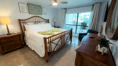 Serene Coastal Bedroom
Elegant rattan bed with crisp white linens and lime accents in airy bedroom. Tropical wall art, ceiling fan, sliding doors to balcony views. Nightstands with lamps, potted plant—peaceful retreat.