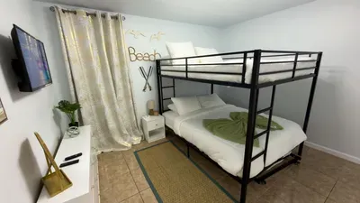 Fun Bunk Bedroom for Beach Bunks
Stylish black metal bunk bed with plush linens in airy kids' room. "Beach" sign, surfboard decor, smart TV, gold drapes, plant accents. Cozy retreat for little adventurers at Royale Beach & Tennis Club.