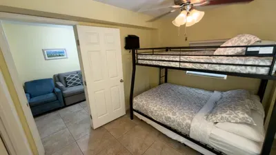 Fun Bunk Room Gateway
Black bunk beds with gray floral linens shine under fan and lights in yellow haven, opening from blue chair lounge. Blinds, AC, coastal art—cheerful family spot adjoining den for easy South Padre access!