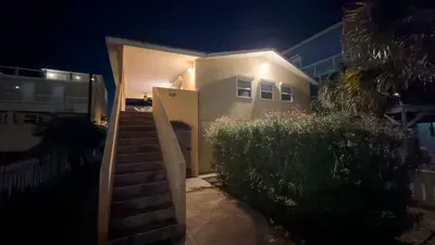 Glowing Yellow Beach Cottage Entry
Warmly lit yellow charmer at night! Elevated stairs, lush landscaping, palm accents—inviting SPI welcome near 113 E Pompano St. Steps to beach, SpaceX launchpad & Gulf waves. Home sweet coastal haven!