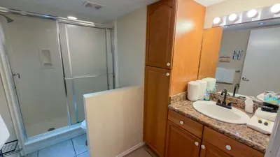 Spacious, well‑kept bathroom featuring a granite vanity with ample storage, bright mirror lighting, organized toiletries, and a clean glass‑door shower—offering guests a comfortable, functional, and thoughtfully maintained space.