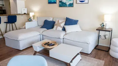 Bright Coastal Living Space
Open‑concept living area with a crisp white sectional, ocean‑inspired décor, hanging chair and a modern kitchen with stainless appliances. A bright, inviting coastal retreat for comfort, connection & effortless vacations.