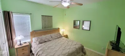 Relax in this cozy, well-lit bedroom featuring a plush serene bed, warm wooden accents, ceiling fan, and smart TV. Thoughtful touches and natural light create a welcoming retreat perfect for restful nights and peaceful mornings.