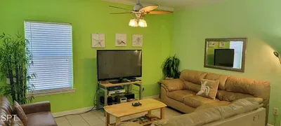 Gather in this bright, welcoming living room with leather sofas, loveseat, coffee table, and flat-screen TV. Natural light, ceiling fan, and tasteful décor create a cozy space perfect for relaxing, entertaining, or family time.