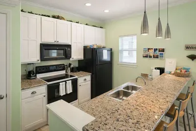 Bright, modern kitchen with granite countertops, stainless steel sink, black appliances, and pendant lighting—perfect for cooking, entertaining, or enjoying a morning coffee at the breakfast bar.