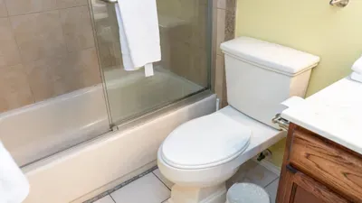 This clean and practical bathroom features a tub/shower combo with sliding glass doors, a toilet, and a vanity with storage. Perfect for refreshing after the beach or pool, it offers all the essentials for a comfortable stay.